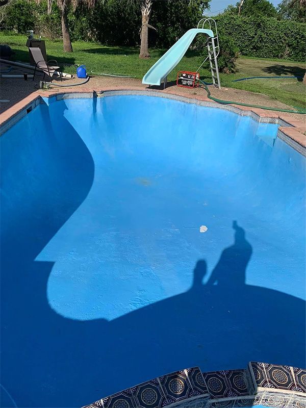 Empty blue swimming pool, with a slide and tools on the deck.