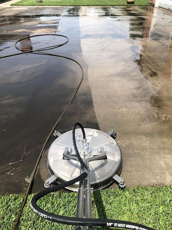 A pressure washer cleaning a dirty concrete driveway, revealing a clean stripe.