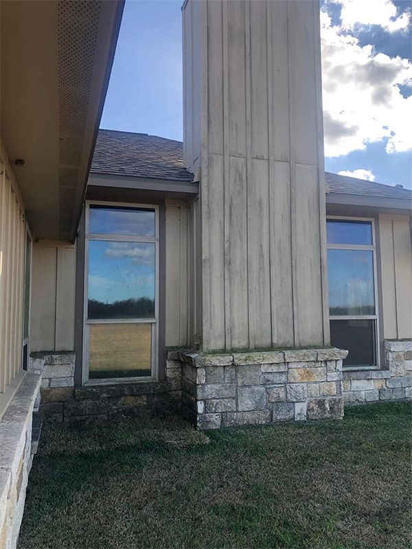 Tall chimney and windows on a building, with light brown siding, a stone base, and blue sky.