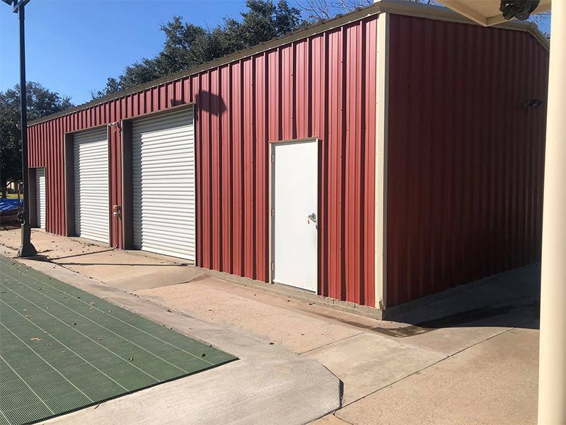 Red metal building with three bays, two garage doors, and a white door.