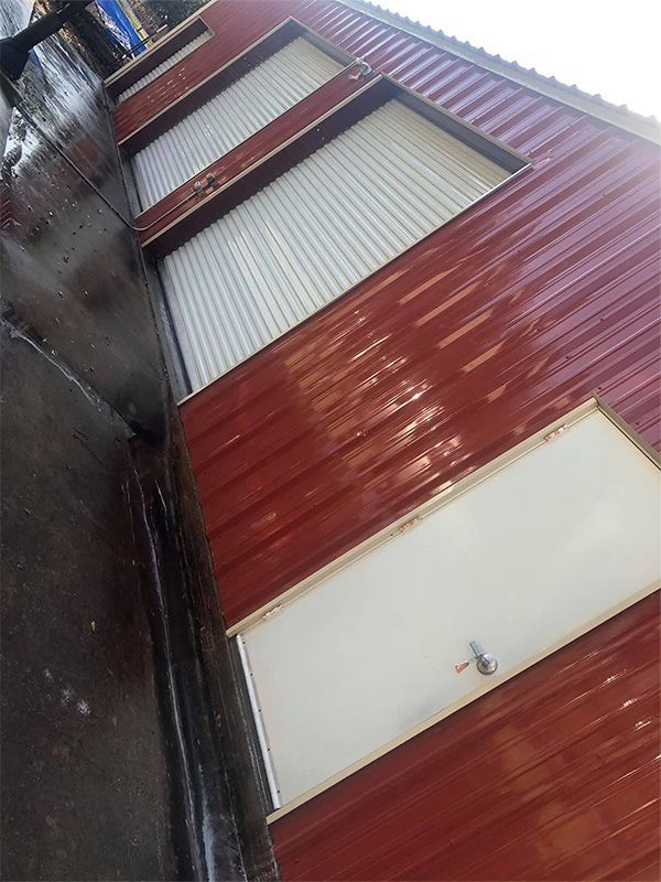 Red corrugated metal building with three roll-up doors and a white door.