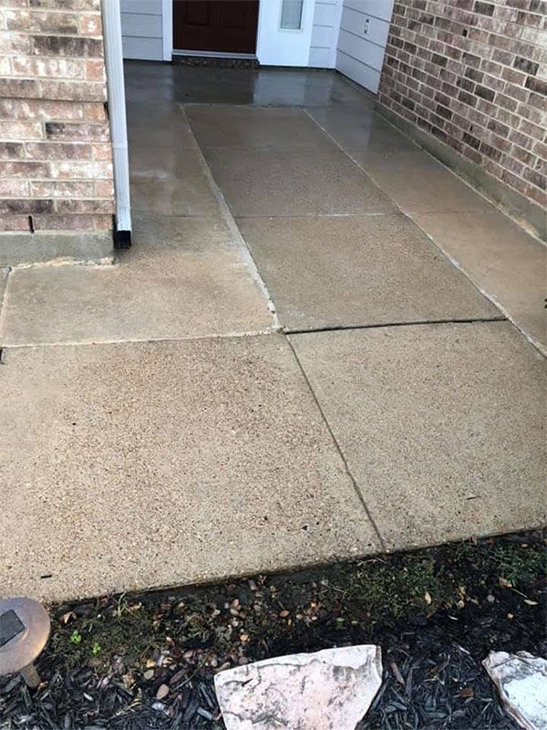 Concrete walkway leading to a front door with a brick and siding exterior. Wet and smooth surface.