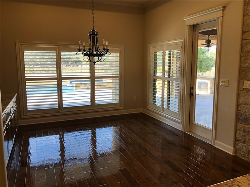 Dining room with hardwood floors, chandelier, shuttered windows overlooking a pool.