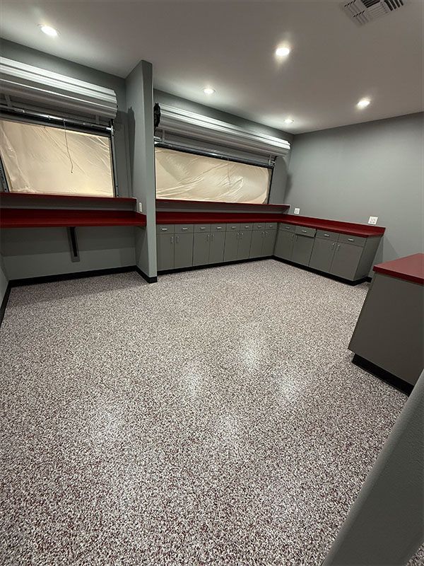 Empty room with speckled flooring, gray cabinets, and red countertops, with shuttered windows.