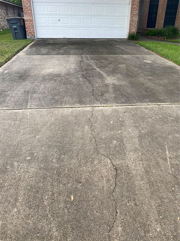 Concrete driveway with visible cracks, stained and dirty, in front of a garage.