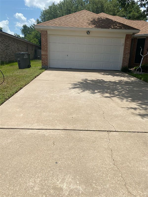 Concrete driveway leading to a white garage door under a brown roof on a sunny day.