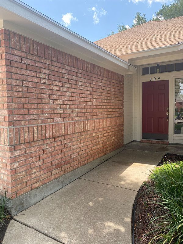 Brick building exterior with red door and concrete walkway.