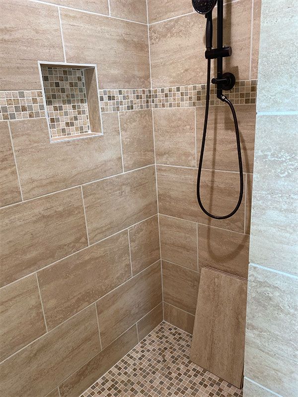 Shower stall with tan tile walls, a mosaic tile border and floor, and black shower fixtures.