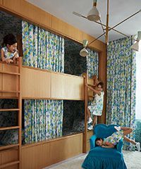 Children in bunk beds with floral curtains and blue armchair.