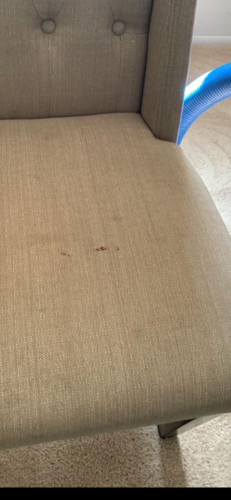 Close-up of a beige upholstered chair seat and back with a button tuft, next to a blue object.