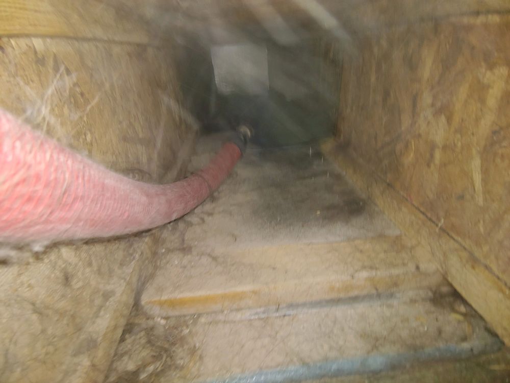 Pink hose inside a dusty vent or duct with narrow steps leading into a dark opening