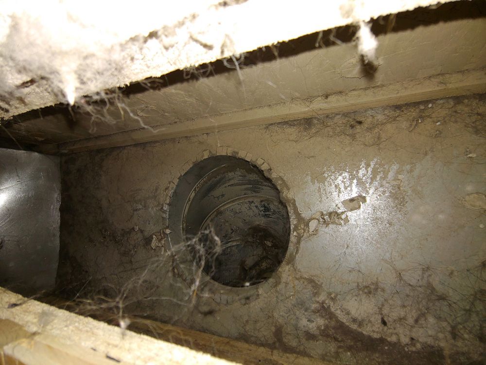 Dusty metal duct opening inside a wall cavity with cobwebs and debris