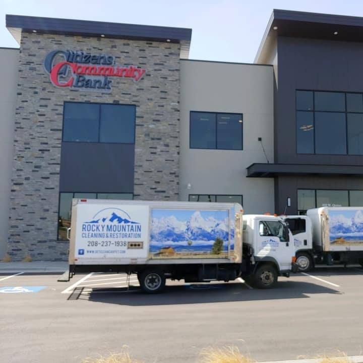 Delivery truck parked outside a bank building with a stone facade and blue windows.