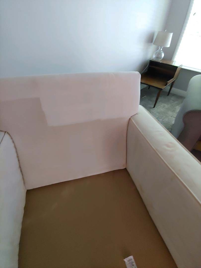 Beige upholstered armchair in a bright room with a small table and chair in the background
