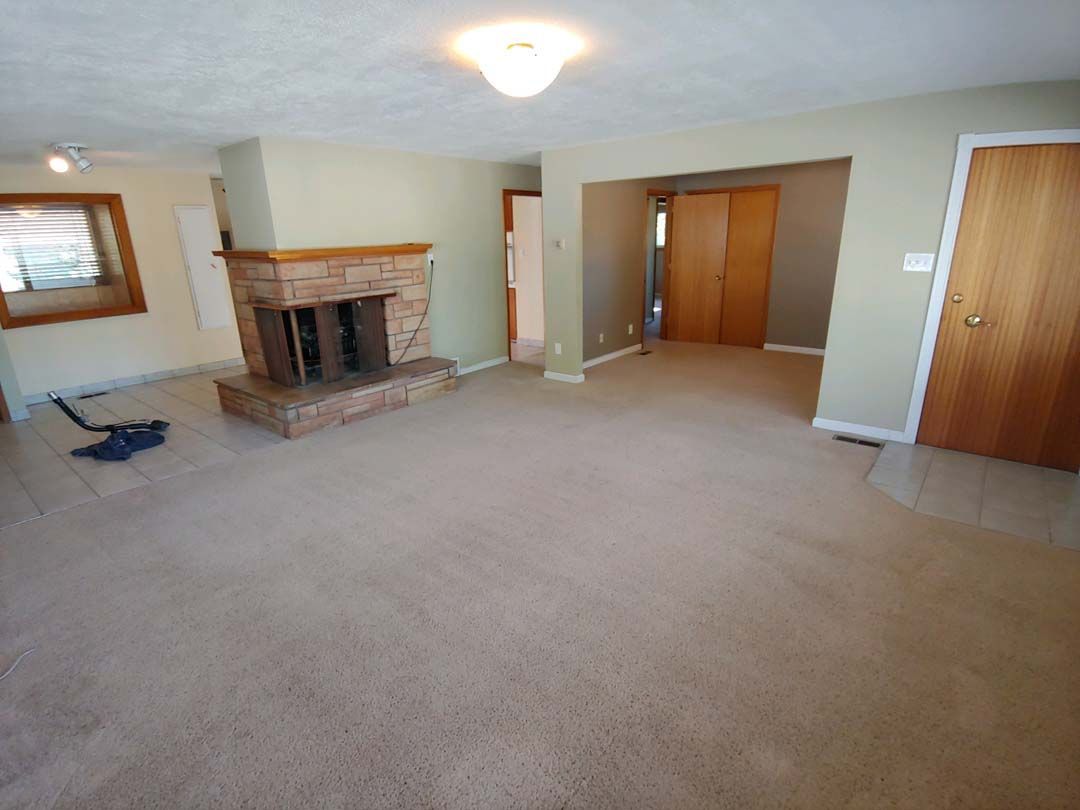 Empty beige living room with fireplace, carpeted floor, and wood doors and trim