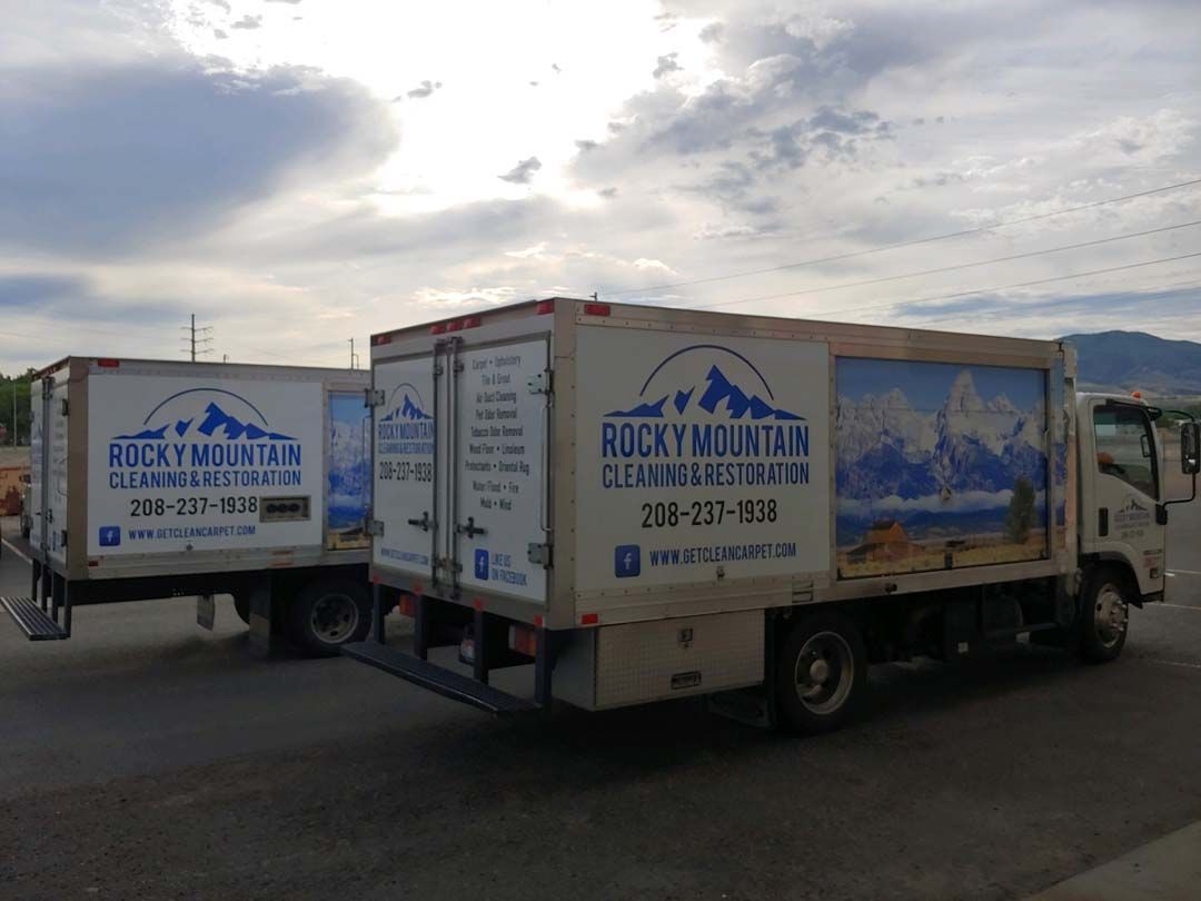 Two Rocky Mountain moving trucks parked outdoors under a cloudy sky