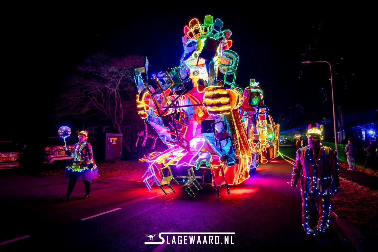 Een praalwagen tijdens een nachtparade met felle neonlichten en deelnemers in kostuums.