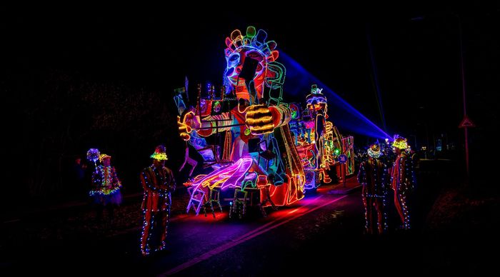 Een stralende, kleurrijke praalwagen 's nachts met artiesten in verlichte kostuums.
