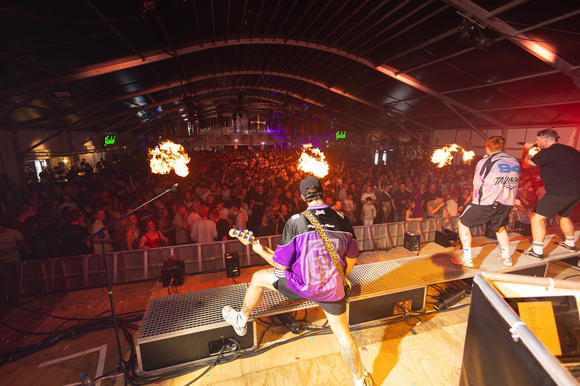 Een band treedt op tijdens een drukbezocht concert. Met vlammeneffecten en podiumverlichting.