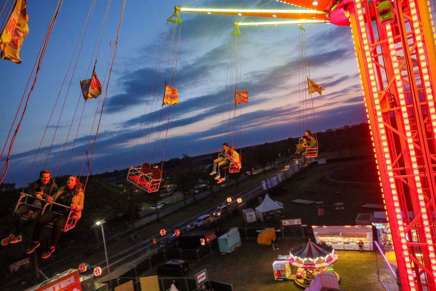 Mensen op een schommelattractie op een kermis in de schemering, verlicht met kleurrijke lampjes.