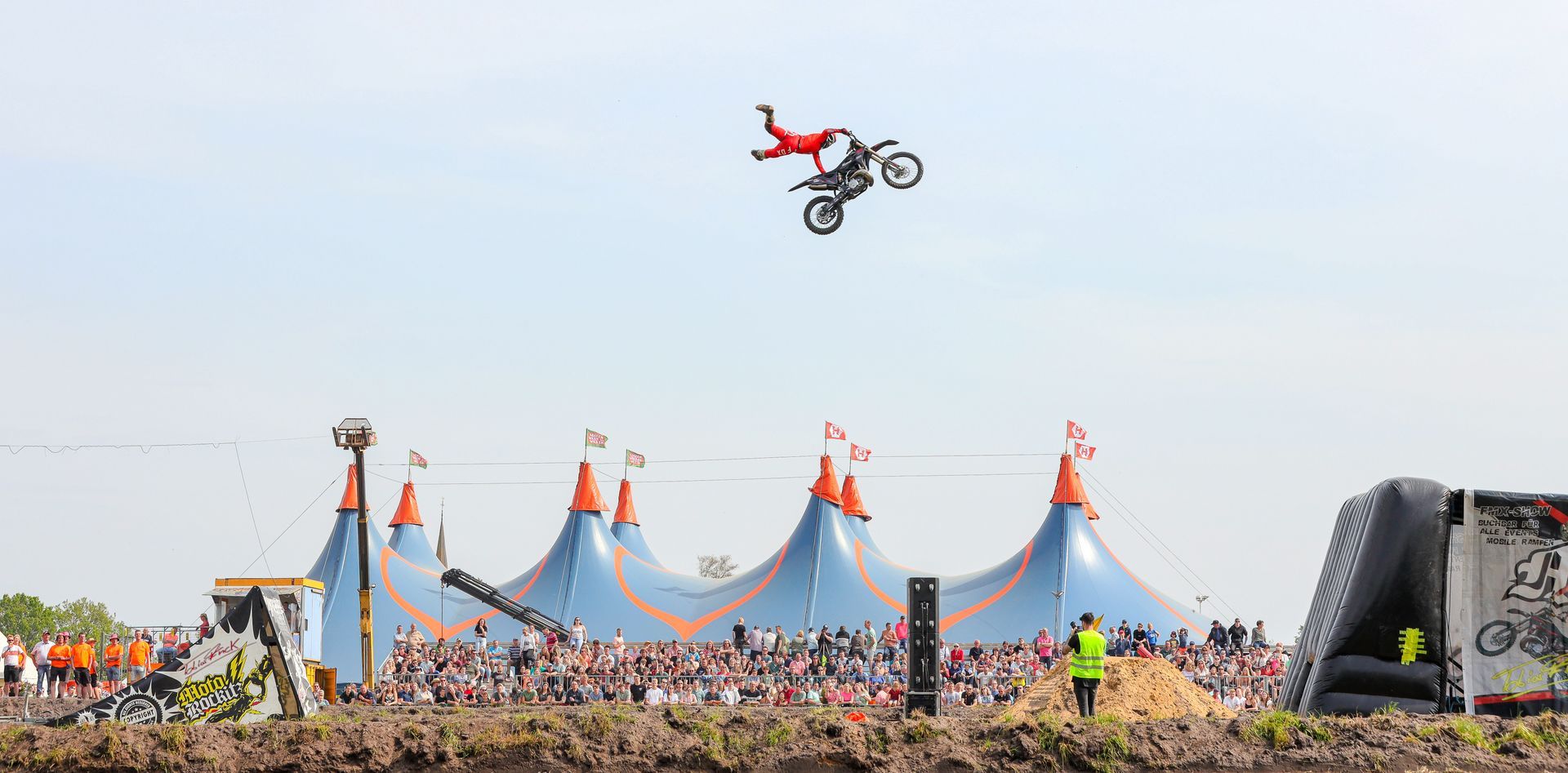 Een motorstuntrijder voert een luchttruc uit boven een menigte in de buurt van een circustent.