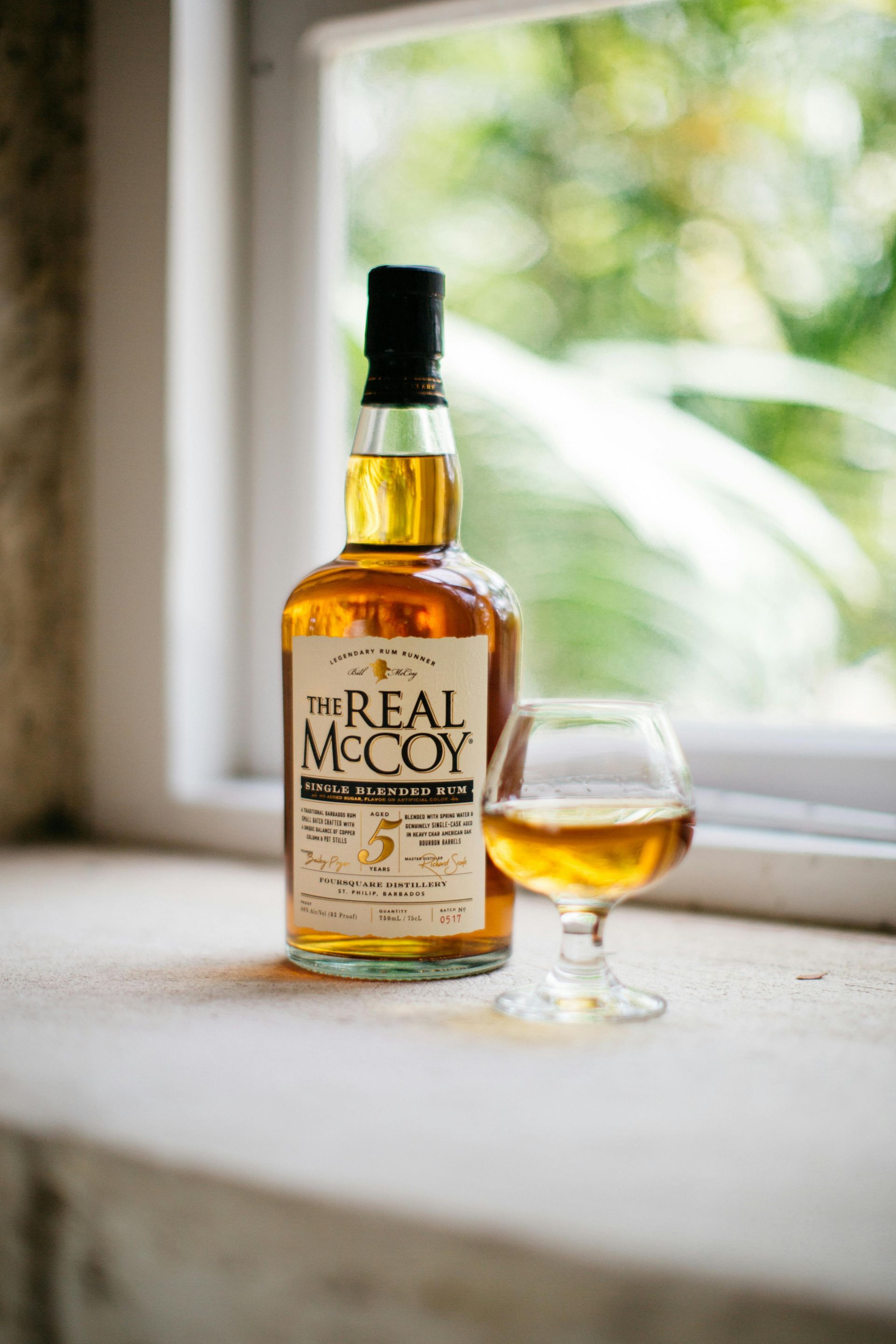 A bottle of whiskey and a glass of whiskey are on a window sill.