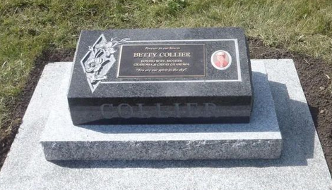 Black granite memorial plaque on a light stone base in a grassy outdoor setting.