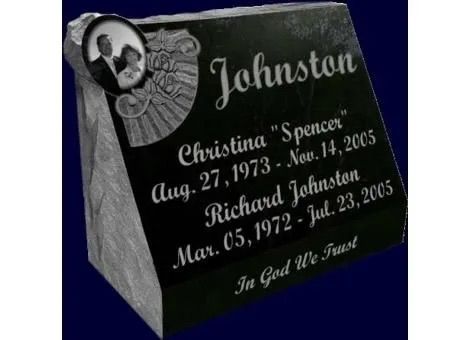 Black granite memorial gravestone with photo medallion and engraved names, dates, and “In God We Trust”
