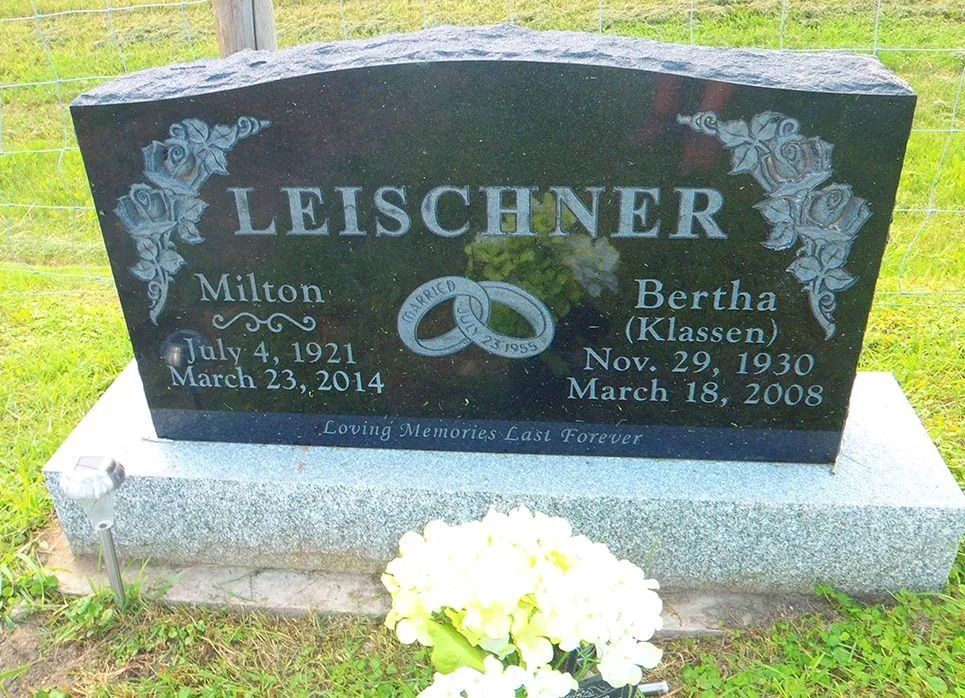 Leischner family gravestone with engraved names, wedding rings, and white flowers at the base