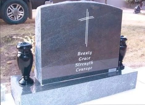 Black granite gravestone with a cross and the words “Beauty Grace Strength Courage” on the front