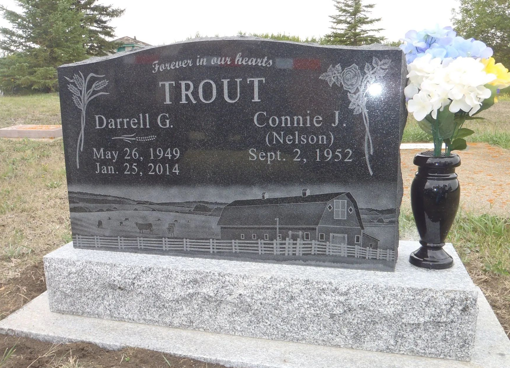 Black granite memorial headstone with white flowers on a stone base outdoors
