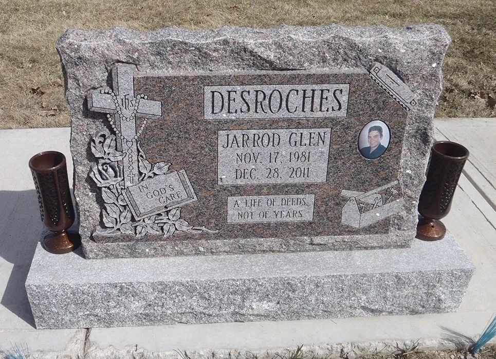 Stone gravestone for the Desroches family with engraved cross and two candle holders.