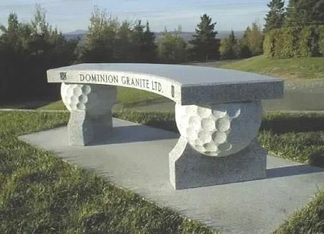 Stone bench with carved grape-cluster supports in a grassy outdoor setting
