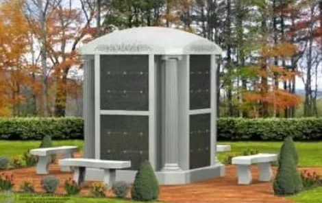 Outdoor memorial with gray columbarium, white benches, and autumn trees in a park