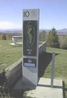 Outdoor golf course marker for hole 10 beside a walkway, with mountains in the background.