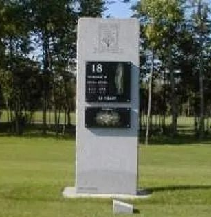 White memorial pillar with plaque and number 18 standing on a grassy lawn, with trees in the background