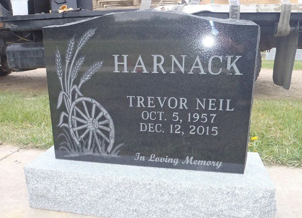 Black gravestone engraved “Harnack” and “Trevor Neil,” with decorative wheat design in a cemetery