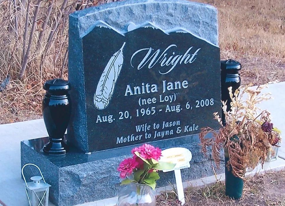 Black granite gravestone with flowers and the name Anita Jane Wright in a cemetery.