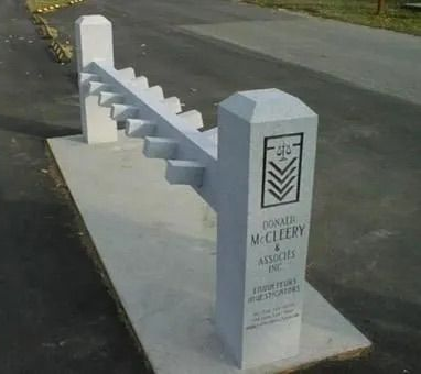 White concrete roadside memorial with stepped design and engraved pillar beside a street