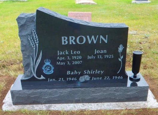 Black granite memorial headstone with engraved names and dates in a grassy cemetery