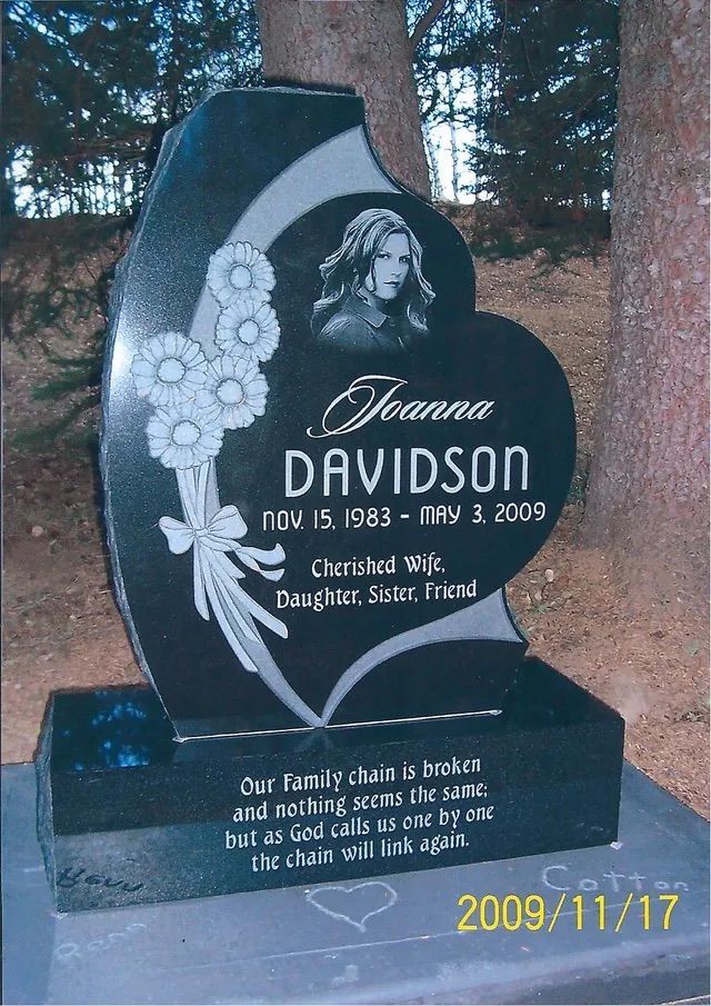 Black granite memorial headstone with a portrait and floral engraving in an outdoor cemetery setting