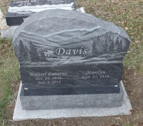 Gray memorial headstone engraved “Davis” with mountain and pine scene in a grassy cemetery.
