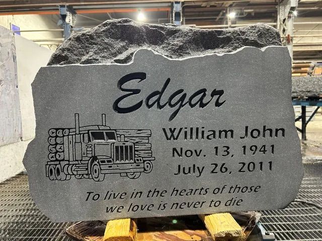 Gray engraved memorial stone with a truck, inscribed “Edgar” and “William John,” in a workshop setting