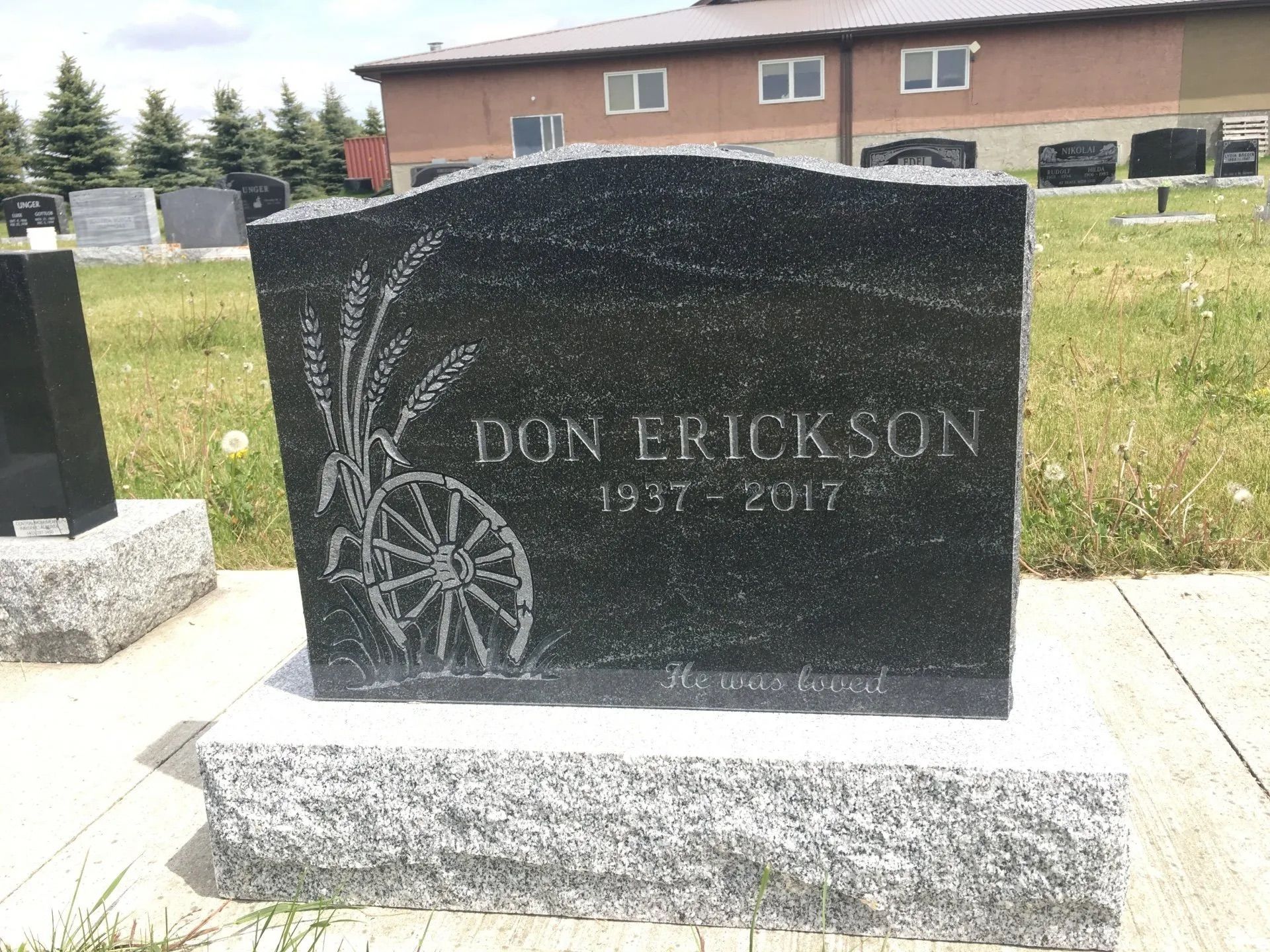 Black granite gravestone with a wagon wheel engraving and the name Don Erickson in a cemetery.