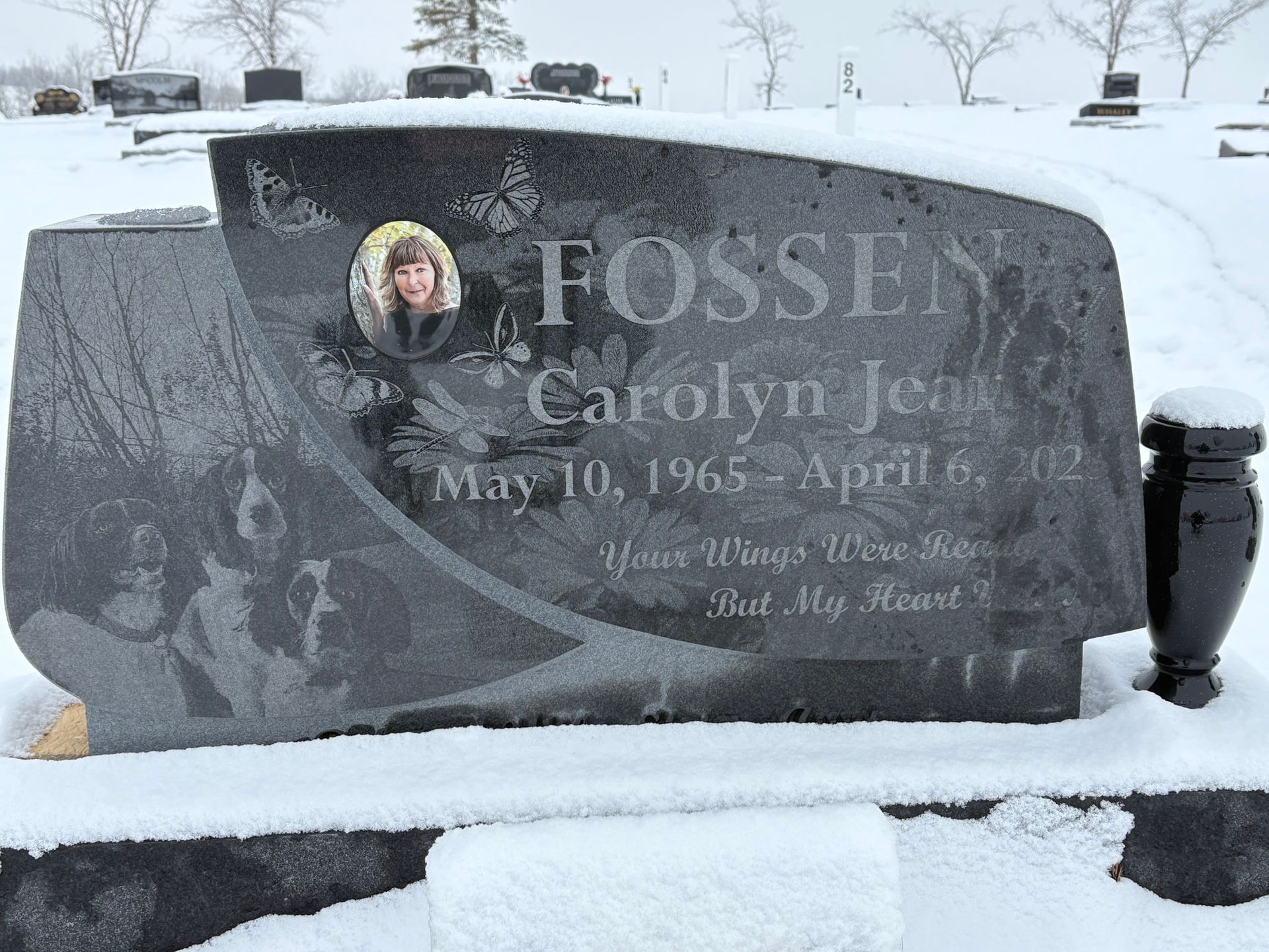 Snow-covered gravestone in a cemetery, engraved with the name Carolyn J. Fossen.