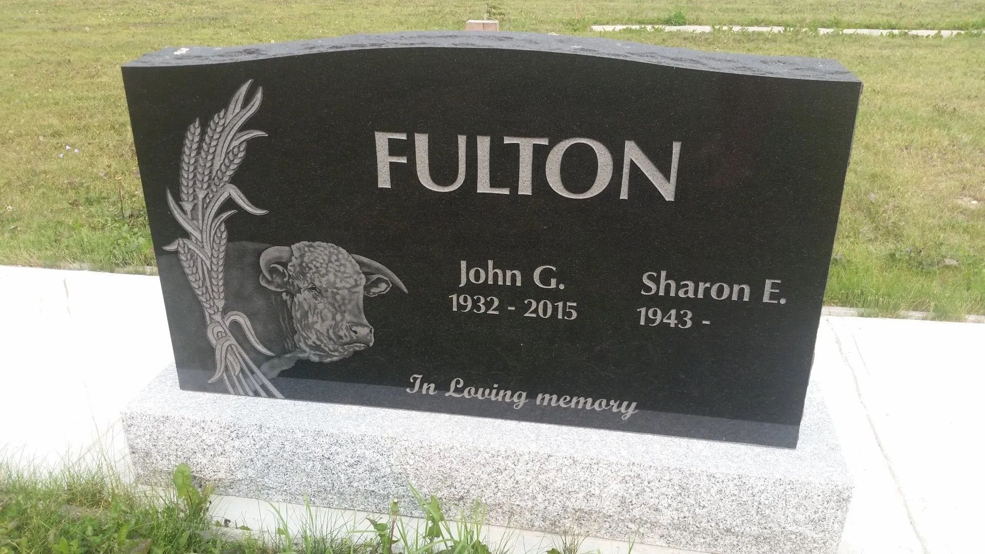 Black Fulton gravestone with floral engraving and the names John C. and Sharon E. in a cemetery