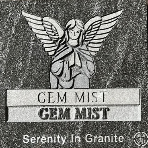 Engraved angel statue with wings above “GEM MIST” and “Serenity In Granite” text on a speckled stone plaque