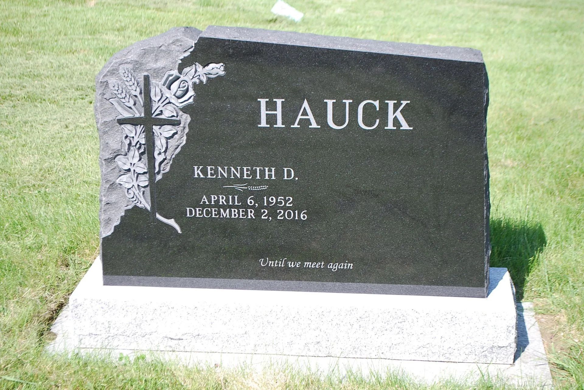 Black granite gravestone with white flowers and the name HAUCK in a cemetery lawn