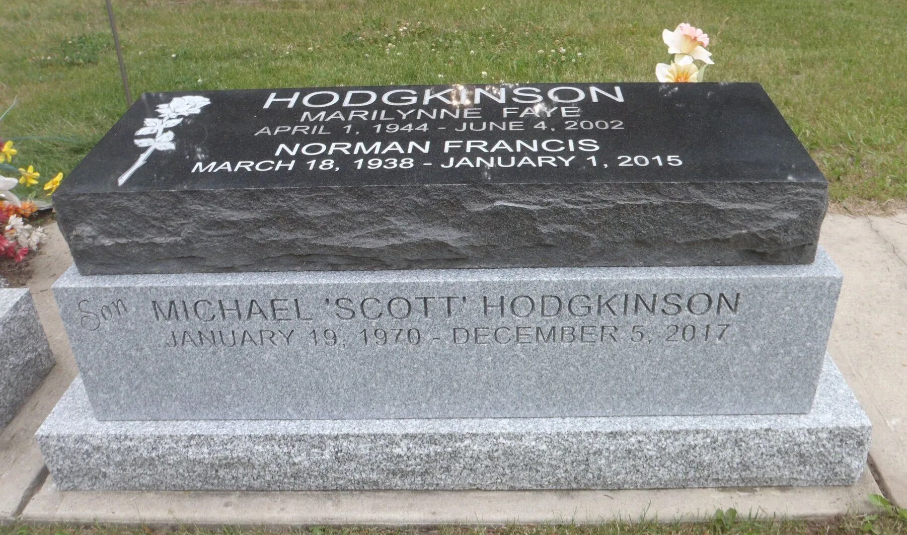 Stone gravestone with engraved names and flowers at a cemetery