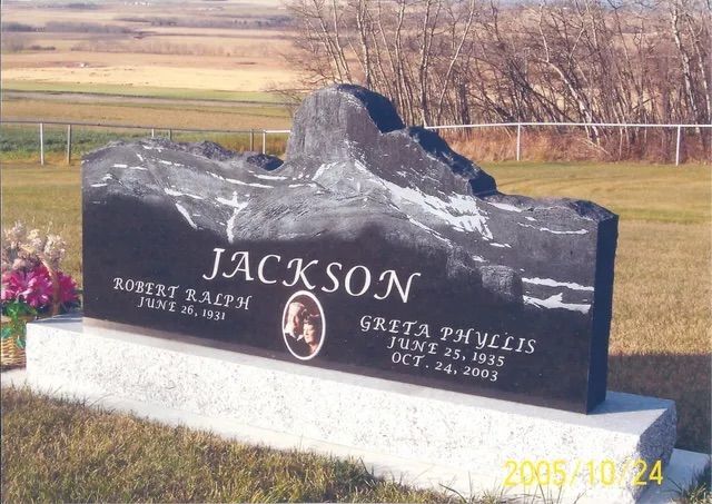 Jackson gravestone on a cemetery lawn with engraved names and dates, set against open fields.